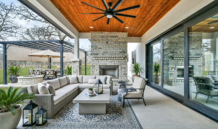 Covered outdoor patio with seating area, fireplace, and garden view.